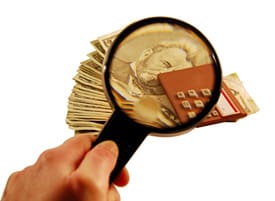 A person holding a magnifying glass over money.